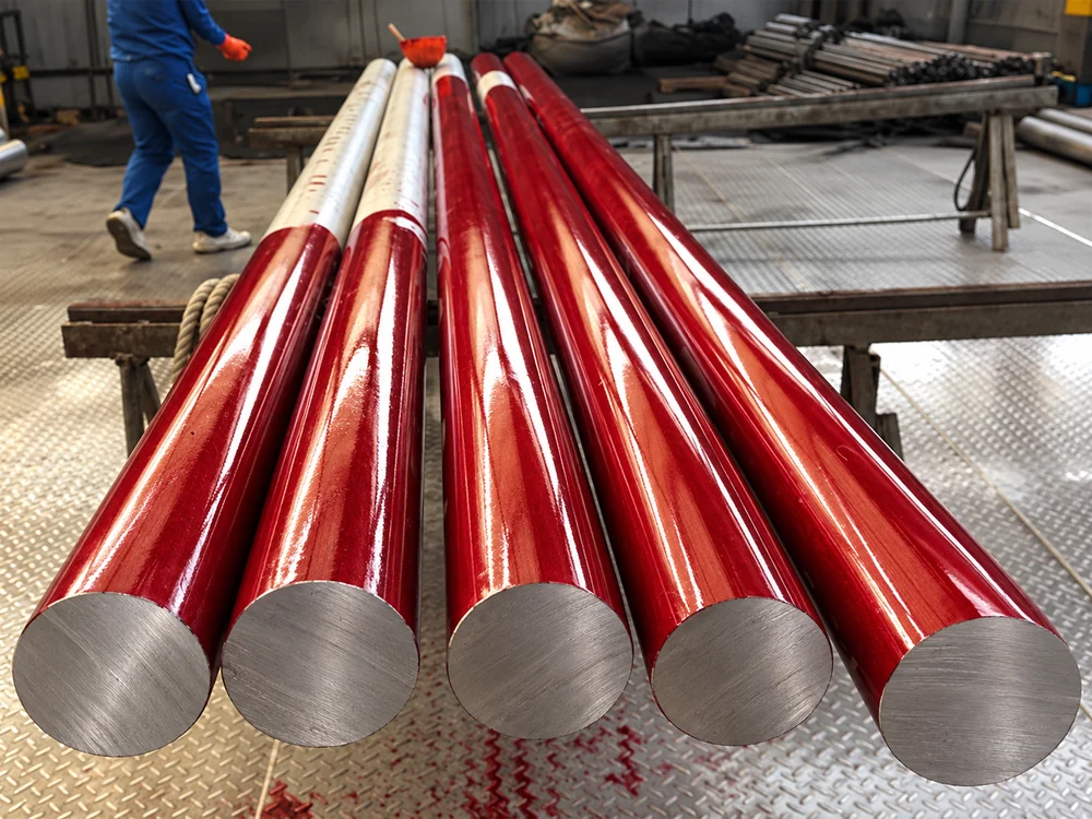 Red liquid penetrant coating on solid round bar surfaces in a workshop